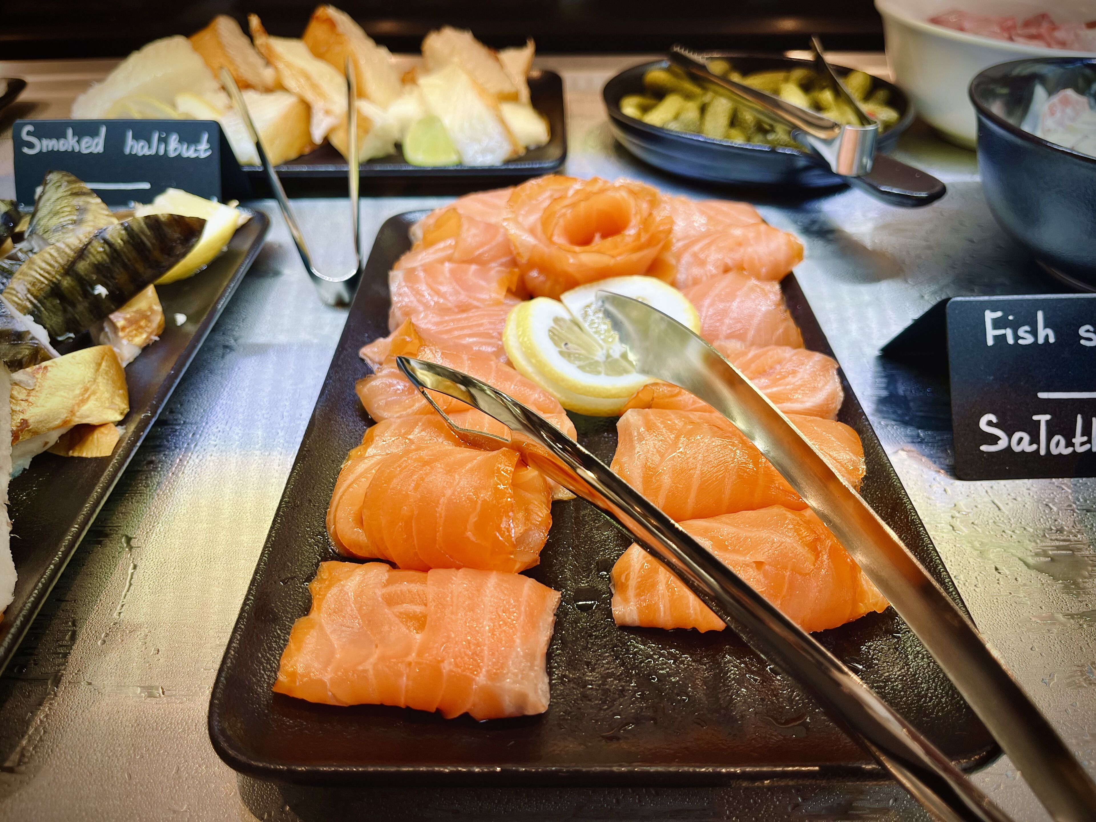 Diverse sushi-bordjes, waaronder gerookte kabeljauw en stukjes vis, op een toonbank.