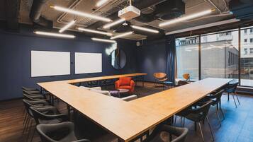 A conference room with a long table, multiple chairs, a projector, and a large window with a city view.