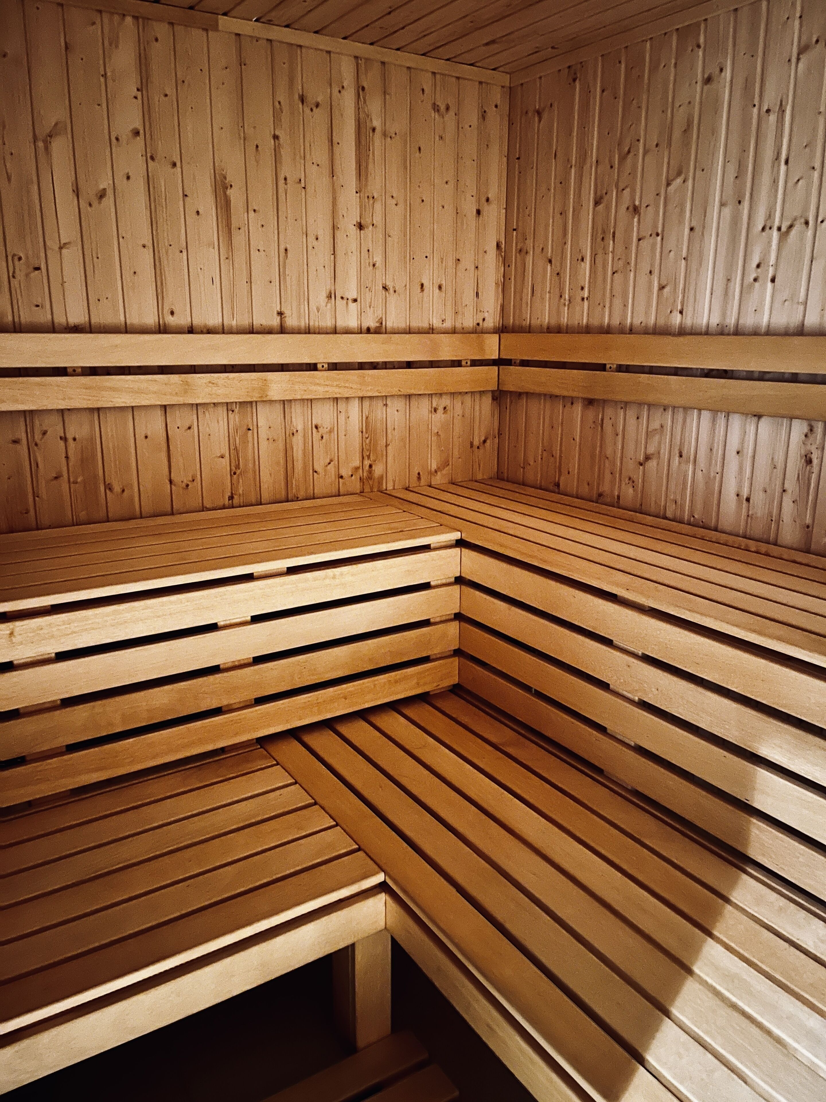 A sauna with wooden benches and walls, featuring a sloped ceiling and a bench at the bottom.