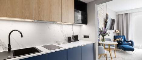 Una cocina moderna con microondas incorporado, un fregadero y una cafetera. Hay una zona de comedor con una mesa y sillas, y un sillón azul.