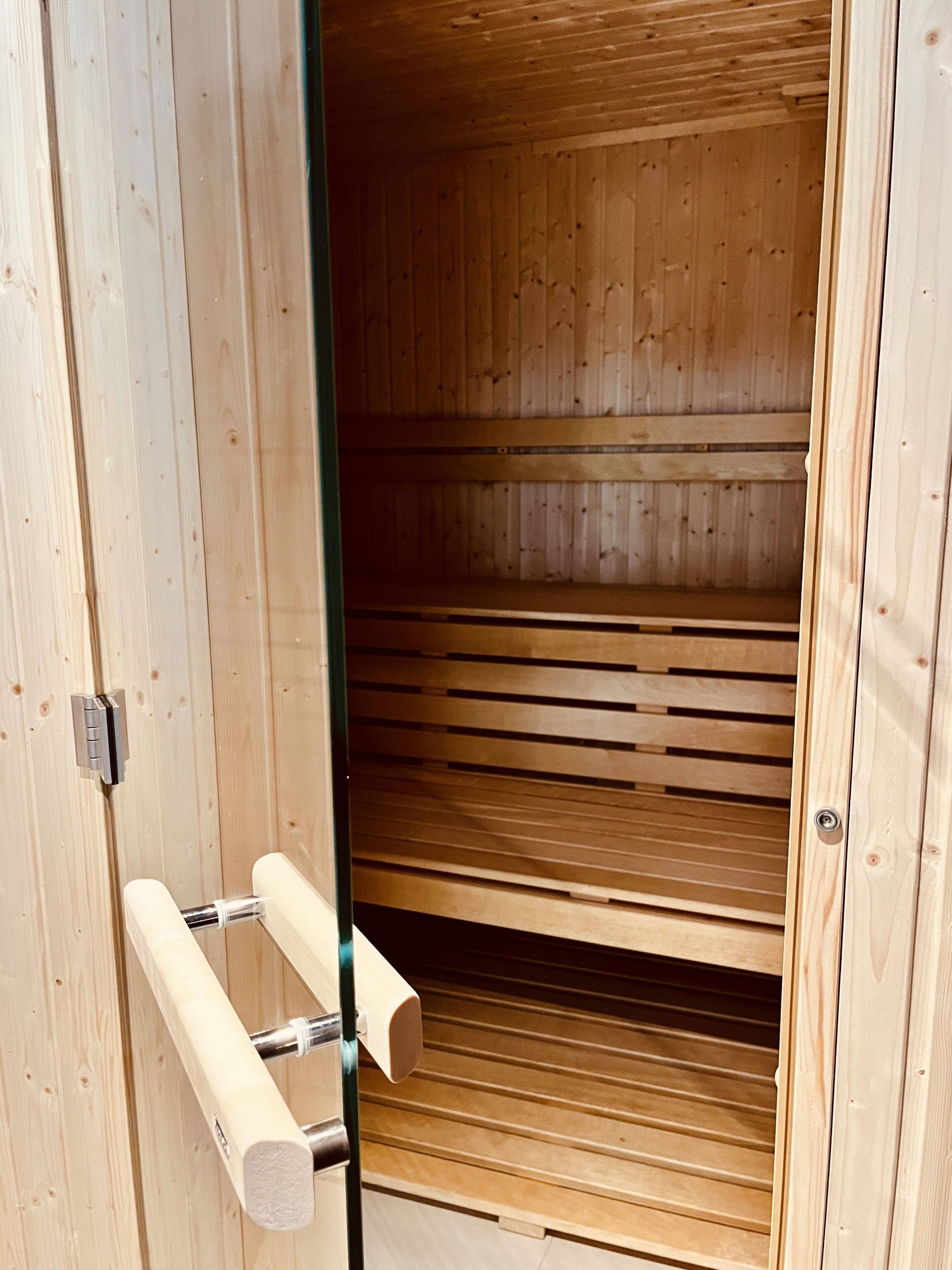 A wooden sauna with a sliding door, a towel rack, and a bench.