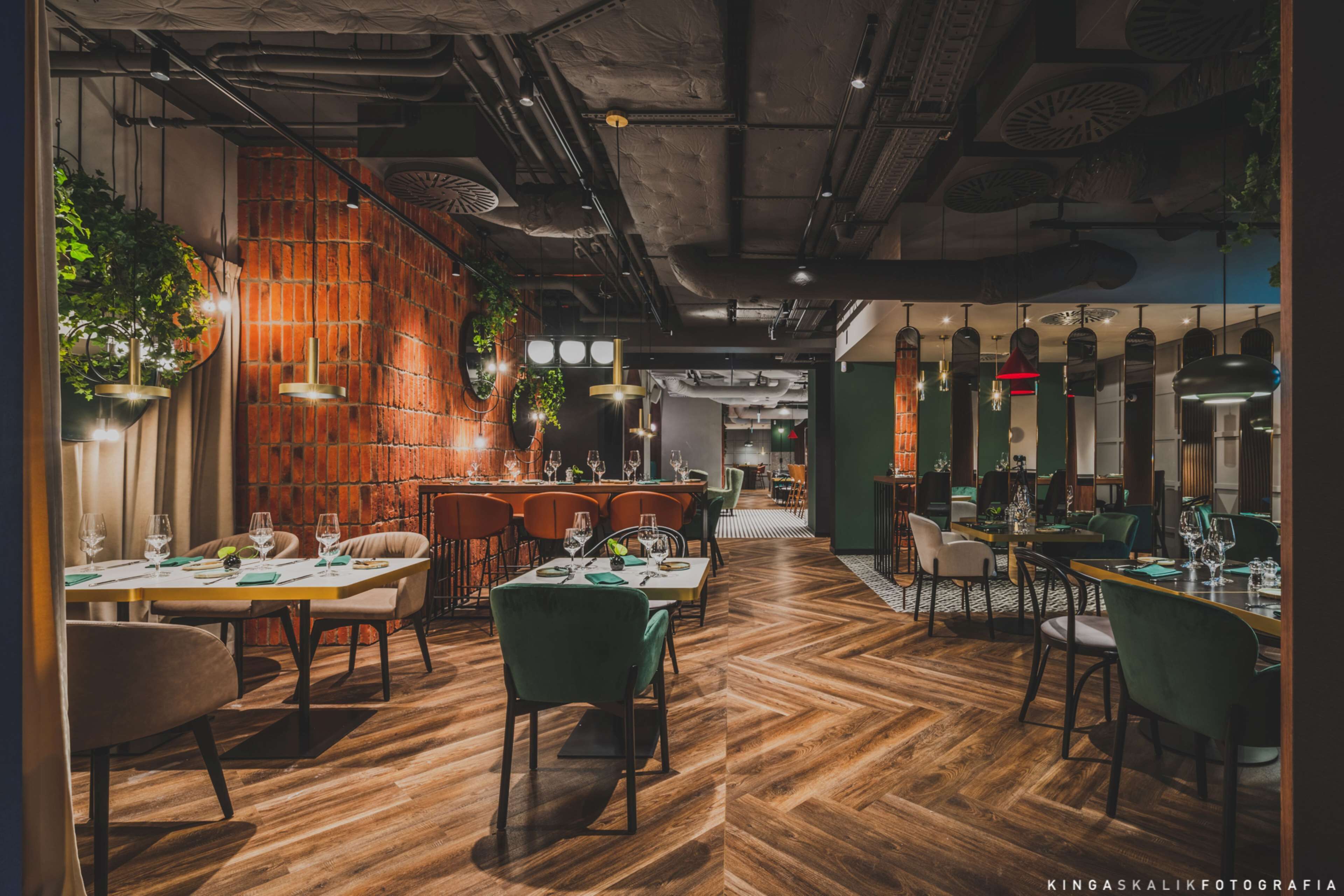 Um restaurante com piso de madeira, cadeiras verdes e plantas pendentes.