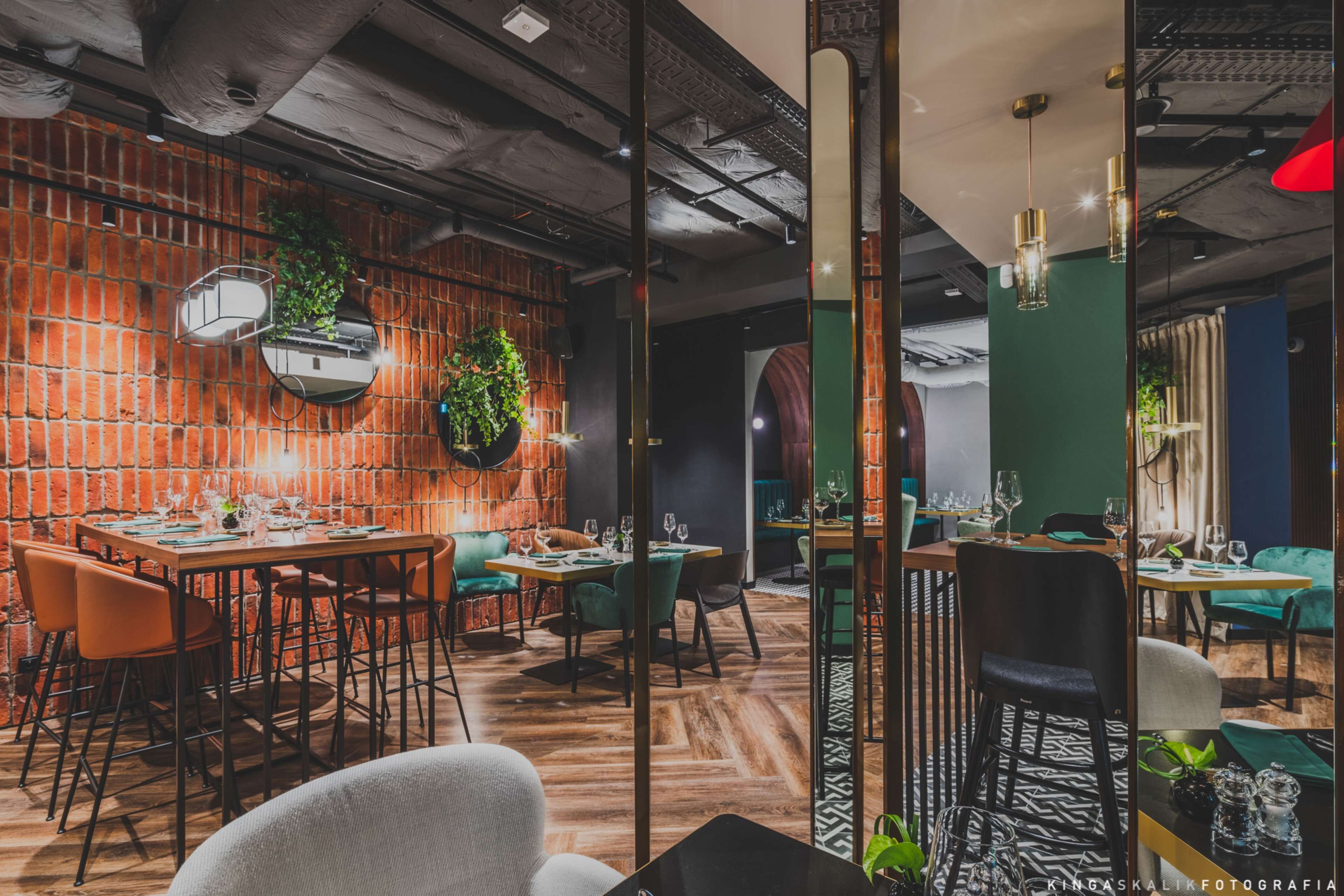 Un restaurant aux murs de briques, aux planchers de bois et aux chaises recouvertes d’un tissu vert.