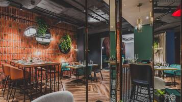 Un restaurant aux murs de briques, aux planchers de bois et aux chaises recouvertes d’un tissu vert.