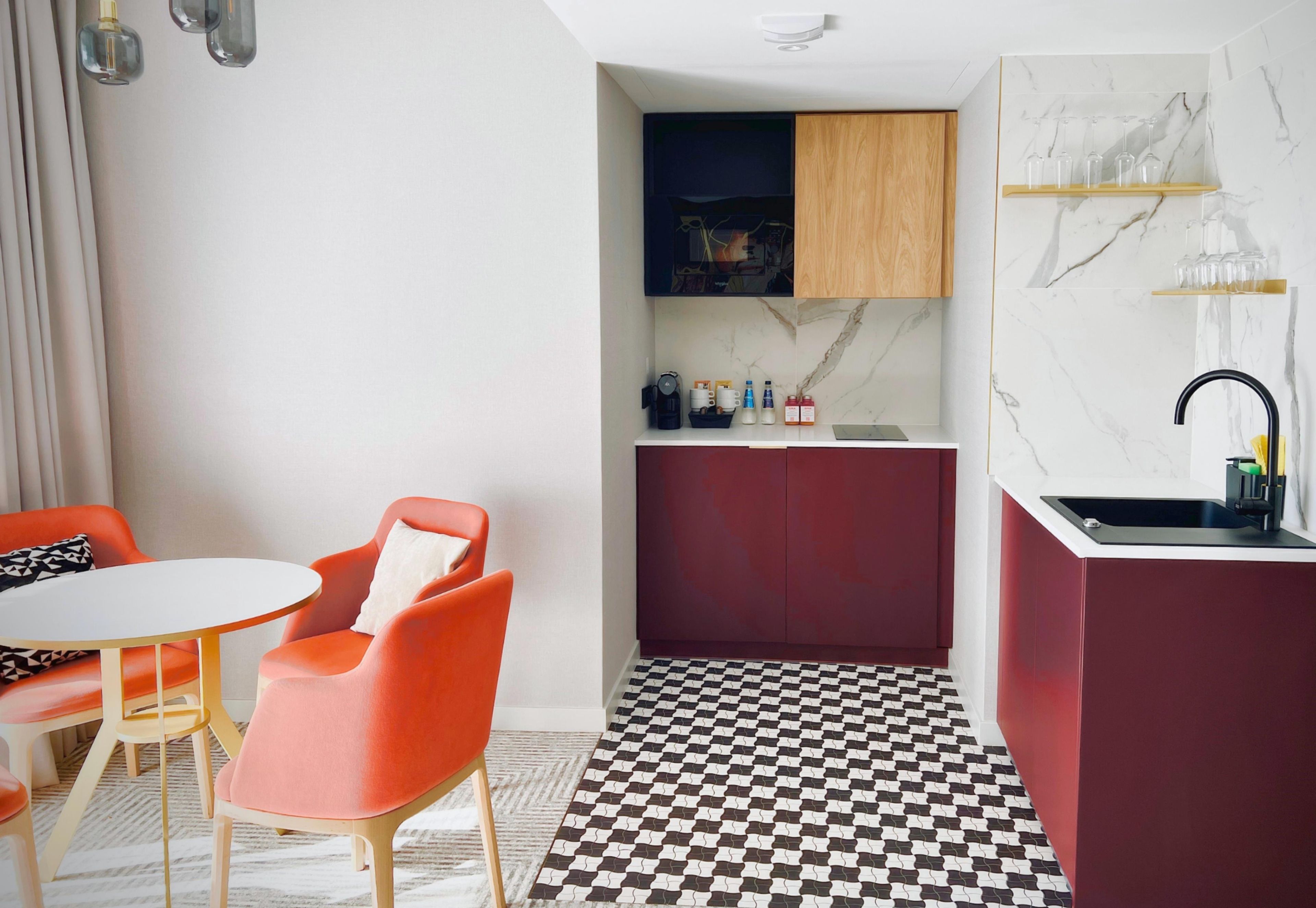 Una cocina compacta con piso a cuadros, una zona de comedor con mesa y sillas, y un pequeño bar con lavamanos.