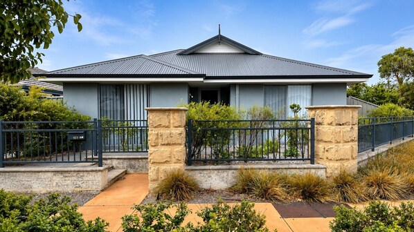 A two-story house with a grey roof, a front porch, and a stone retaining wall. - Napolean Holiday Retreat (Kealy)