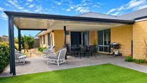 Eine überdachte Terrasse mit Gartenmöbeln, einem Grill und einem gepflegten Rasen.