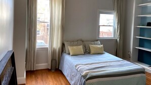 Une chambre à coucher avec un lit, des rideaux, un ventilateur de plafond et une fenêtre.