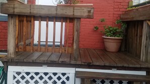 Une terrasse en bois avec une clôture blanche à treillis, un mur en briques rouges et des plantes en pot.