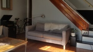 Un salon avec un canapé gris, un plancher en bois, une table basse, une lampe, un vélo et un escalier avec une rampe en bois.