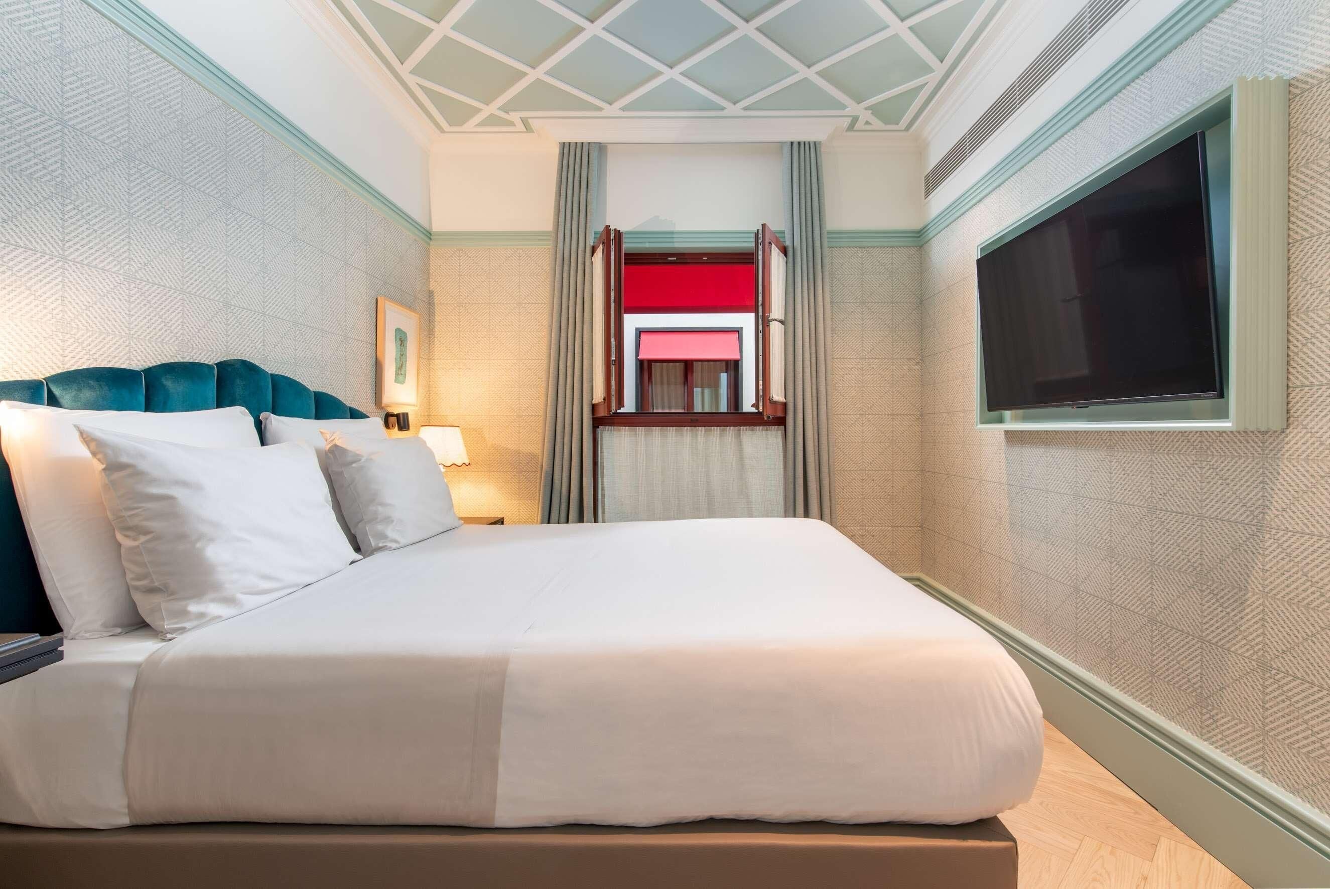 Ein Hotelzimmer mit Bett, einem an der Wand befestigten Fernseher, einem Fenster und Blick auf eine rot-weiße Struktur draußen.