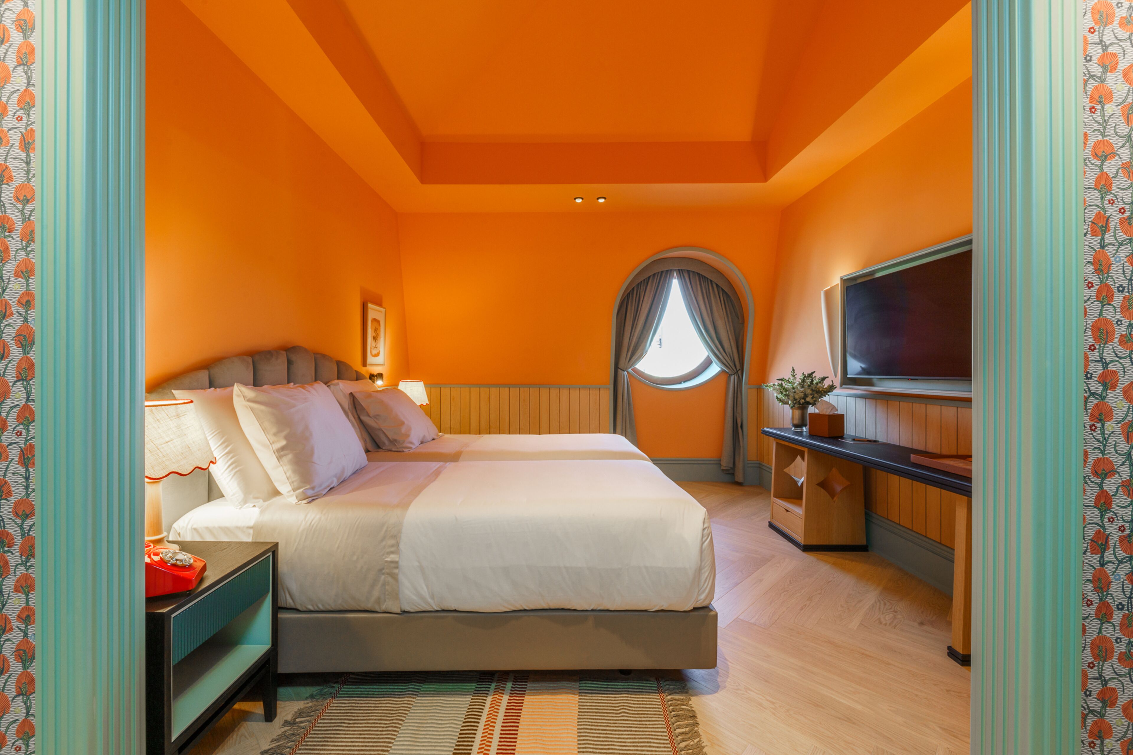 A bedroom with a bed, bedside table, TV, and a window with curtains.