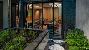 Un bâtiment moderne doté d’une façade originale en forme d’écailles de poisson, d’une entrée en verre et d’un espace de restauration avec des tables et des chaises.