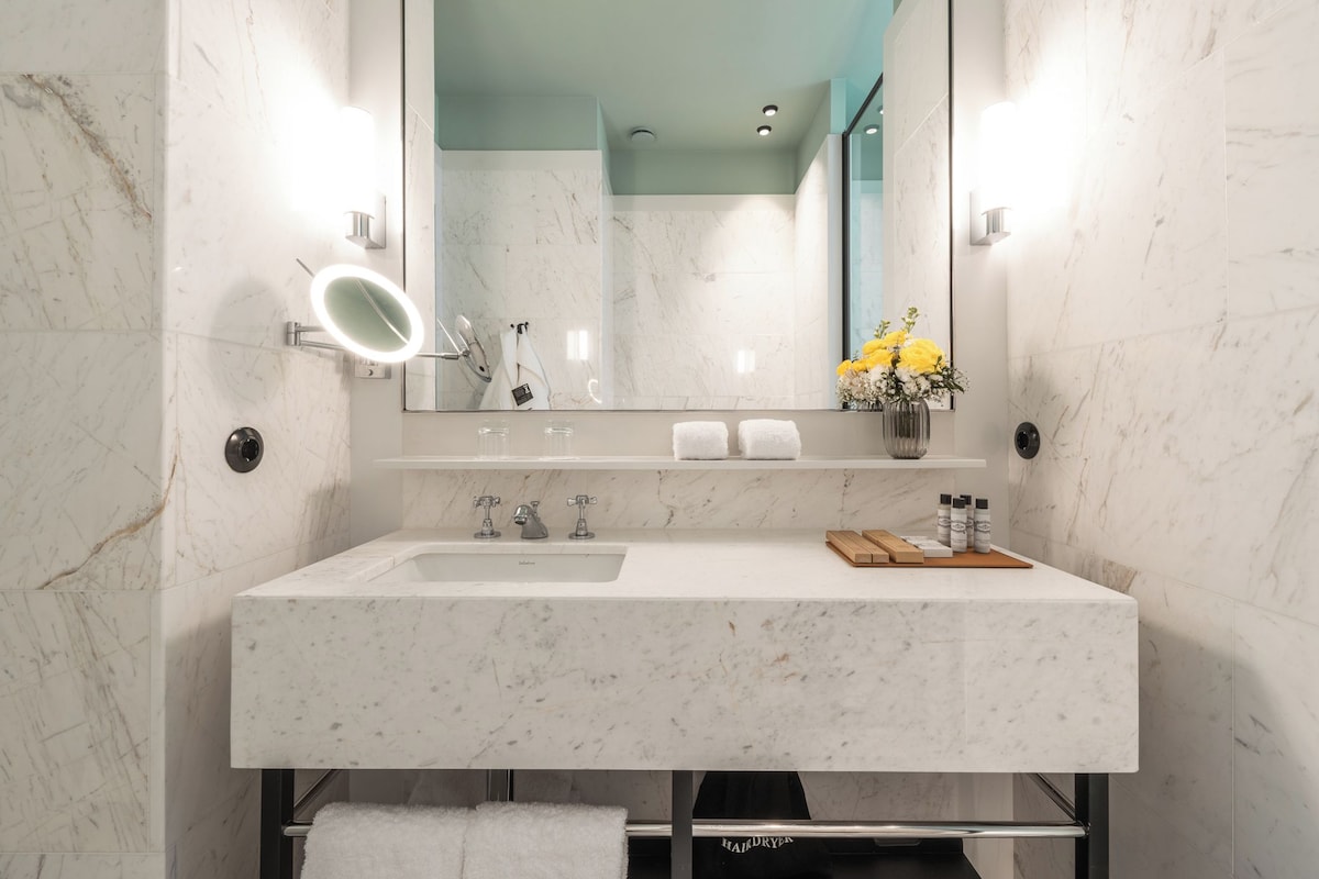 Een moderne badkamer met een grote spiegel, witte marmeren wanden, een wastafel met een houten dienblad en een handdoekhouder.