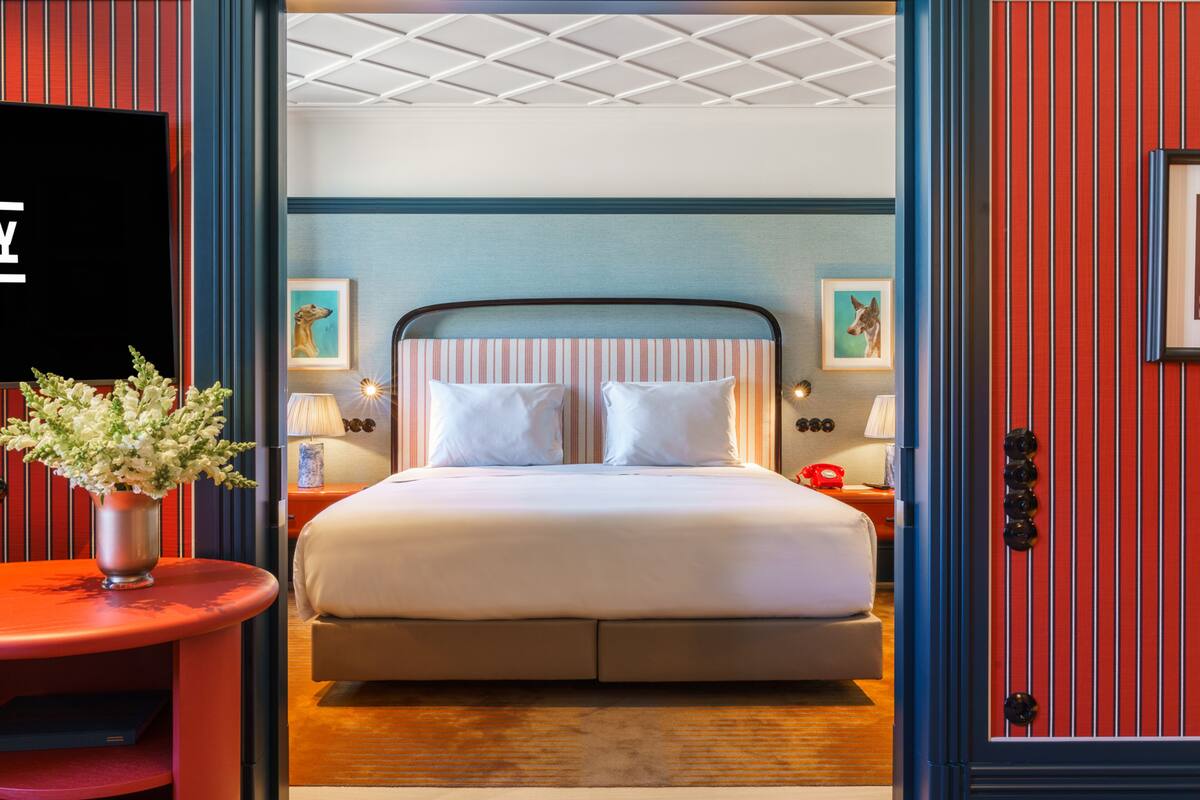 Una habitación de hotel con cama, mesitas de noche, televisión y obras de arte en las paredes.