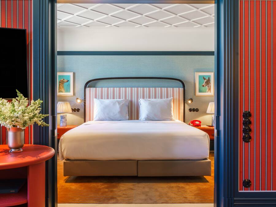 Una habitación de hotel con cama, mesitas de noche, televisión y obras de arte en las paredes.
