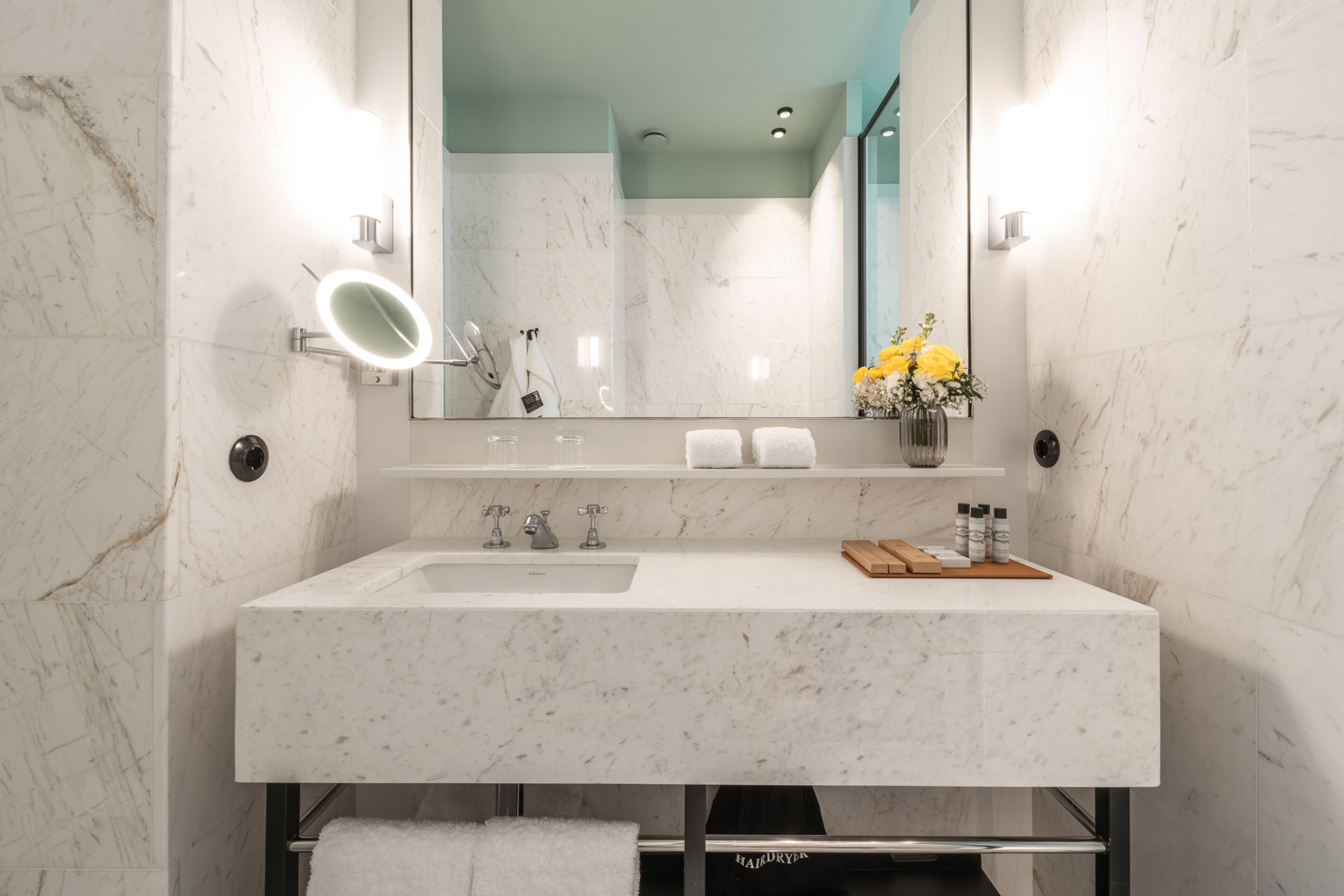 A modern bathroom with a marble sink, a large mirror, and a vase of yellow flowers.