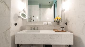 A modern bathroom with a marble sink, a large mirror, and a vase of yellow flowers.