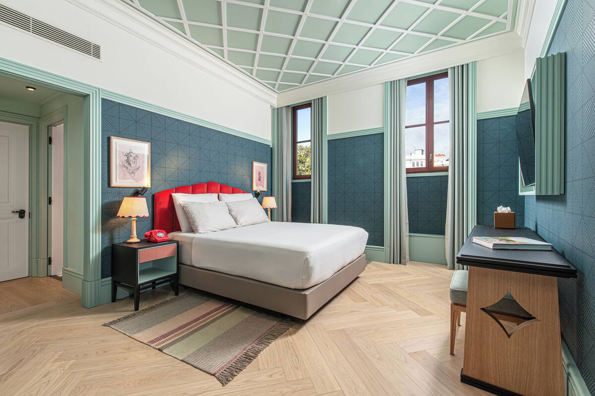 Un dormitorio con cama, mesitas de noche, un escritorio y una ventana.