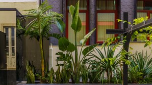 Une cour avec une piscine, entourée de différentes plantes et d’un bâtiment doté d’auvents rouges.