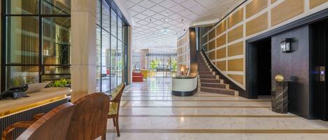 Un amplio vestíbulo con suelo de mármol, un mostrador de recepción y una escalera que conduce a los pisos superiores.