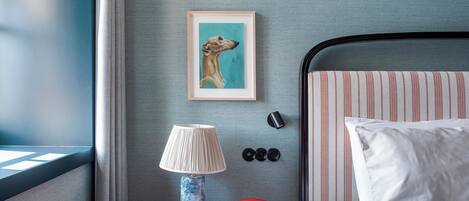 Hotelkamer met een bed, nachtkastje met lamp, een ingelijste foto en een rode telefoon.