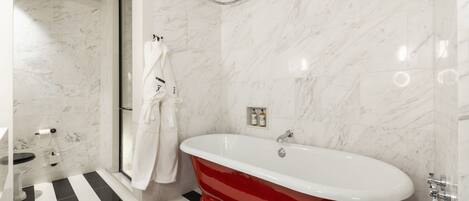 A modern bathroom with a red clawfoot bathtub, a glass shower enclosure, and a black and white striped floor.
