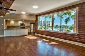 A modern kitchen with a large window overlooking a beach and palm trees. - The Islander 705 - Beachview - Complimentary Beach (Seasonally) - Heated Pool (Destin)