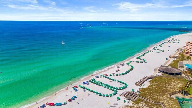 Luchtbeeld van een strand met helder turquoise water, een zeilboot en een rij strandparasols.