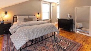 A bedroom with a bed, nightstands, a dresser, a mirror, and a patterned rug.