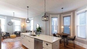 A modern kitchen with a central island, pendant lighting, and a dining area with a round table and chairs.