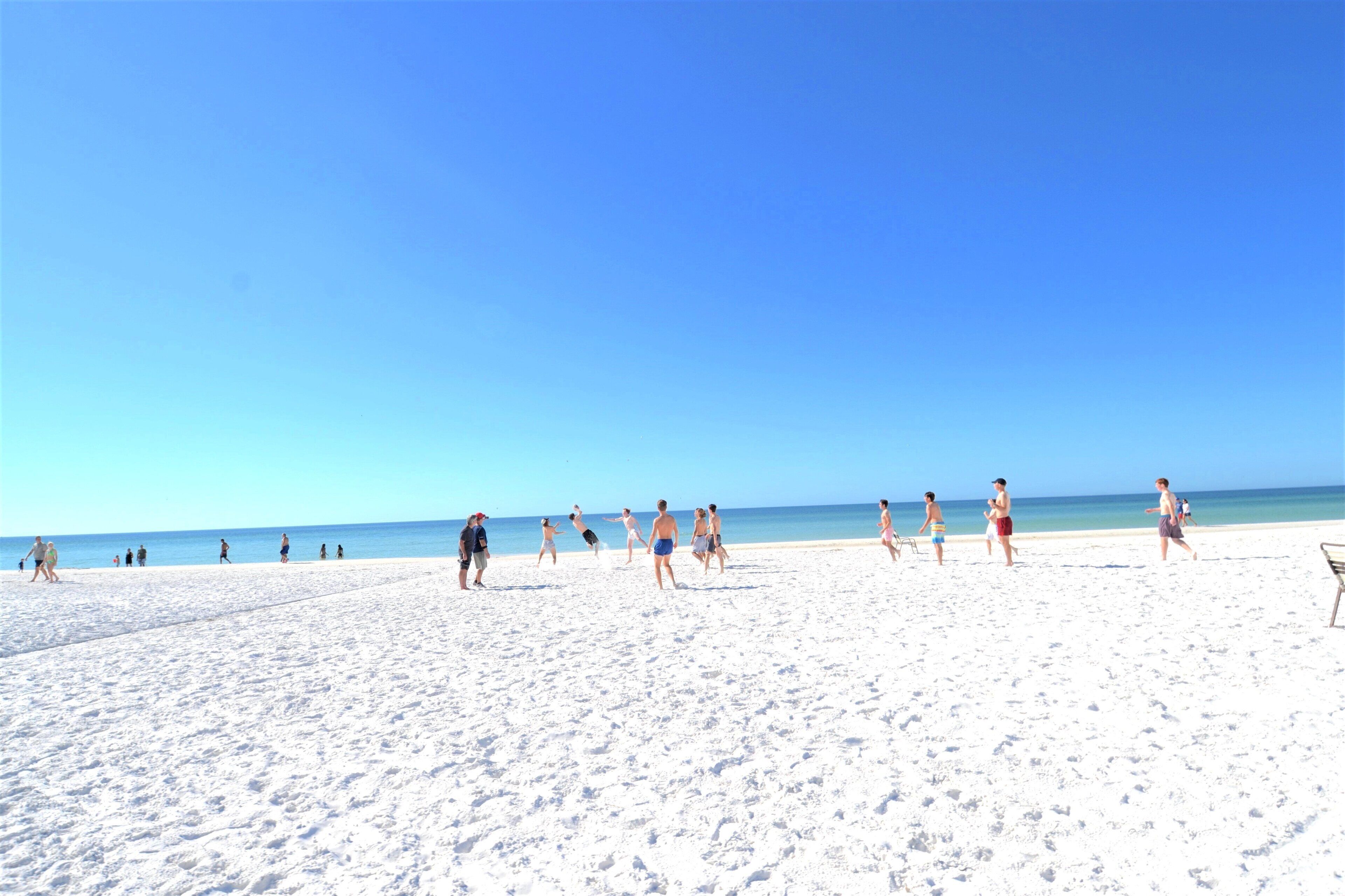 A sandy beach with people walking and playing.