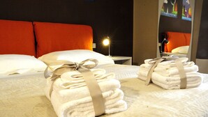 Un lit bien fait, avec du linge de lit blanc et un ruban beige, une lampe de chevet et une tête de lit rouge.