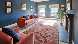 Ein Wohnzimmer mit blauer Wand, einem roten Sofa, einem gemusterten Teppich und einem Kamin.