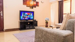 Een woonkamer met een flatscreen televisie, een bank, een salontafel en een decoratieve vaas met bloemen.