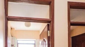 Un couloir étroit mène à une salle de bain équipée de toilettes, d’une petite fenêtre et d’une porte.