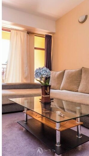 Een moderne woonkamer met een glazen salontafel, een bank en een plant in pot.