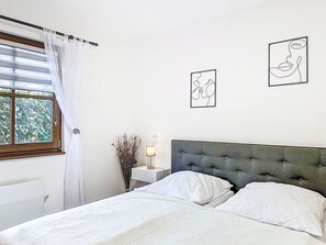 A bedroom with a bed, white bedding, a nightstand with a lamp, and two wall art pieces. - Schwesterchen by Interhome (Frankenau)