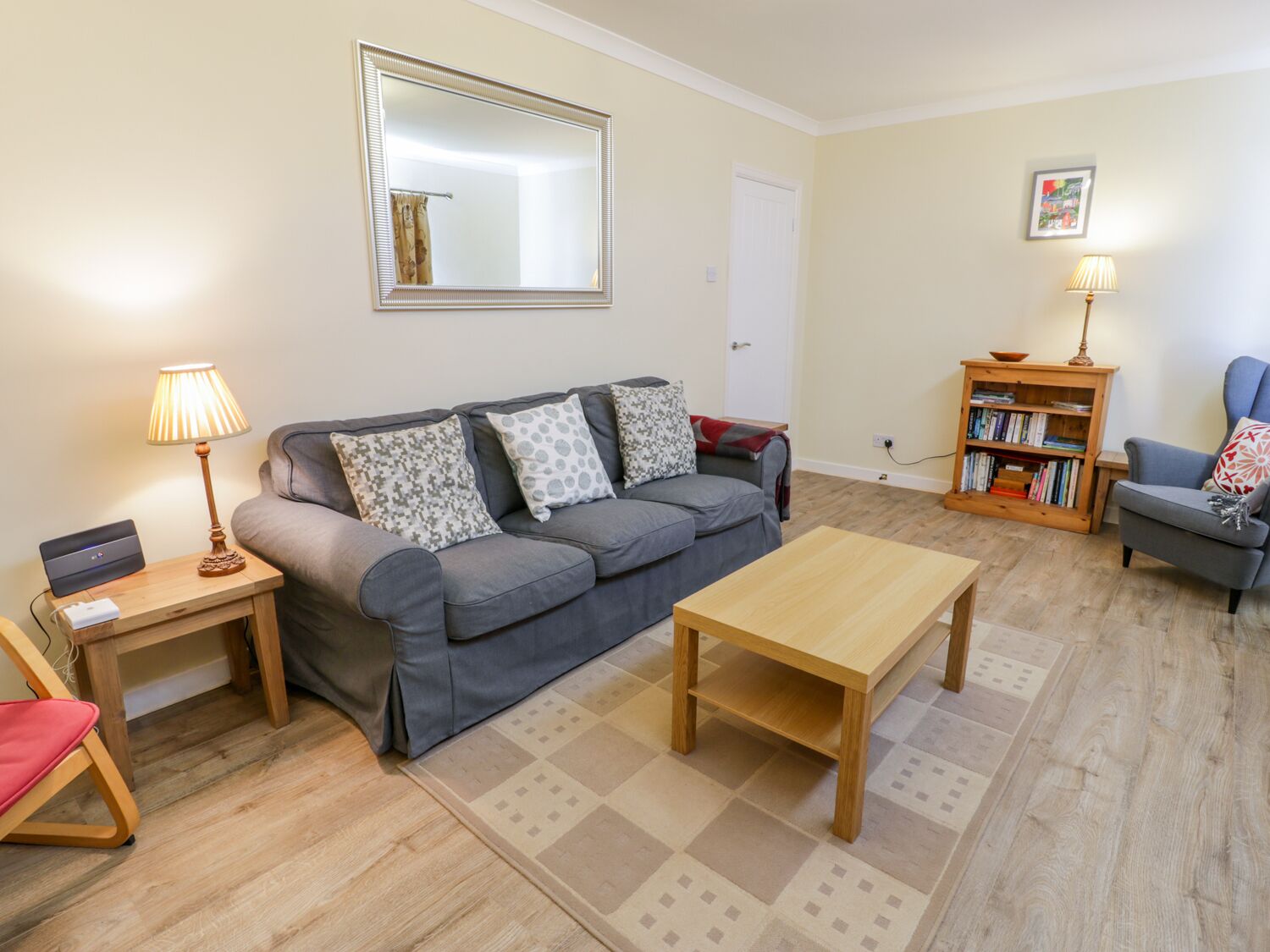 A living room with a grey sofa, a wooden coffee table, a bookshelf, and a lamp.