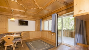 A wooden cabin interior with a dining area, a television, and a sliding glass door to a balcony. - Valle Aurina, Appartement Sonneck Möseler (Lappach)