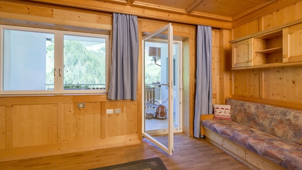 A wooden cabin interior with a sofa, a sliding glass door leading outside, and a small wooden shelf. - Valle Aurina, Appartement Sonneck Möseler (Lappach)