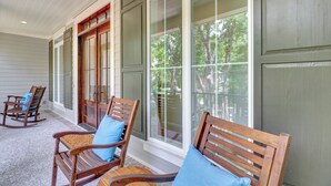 A porch with wooden rocking chairs and a bench, featuring large windows and a wooden door. - Brand New Construction 3rd Row Home in Palmetto Dunes! (Hilton Head Island)