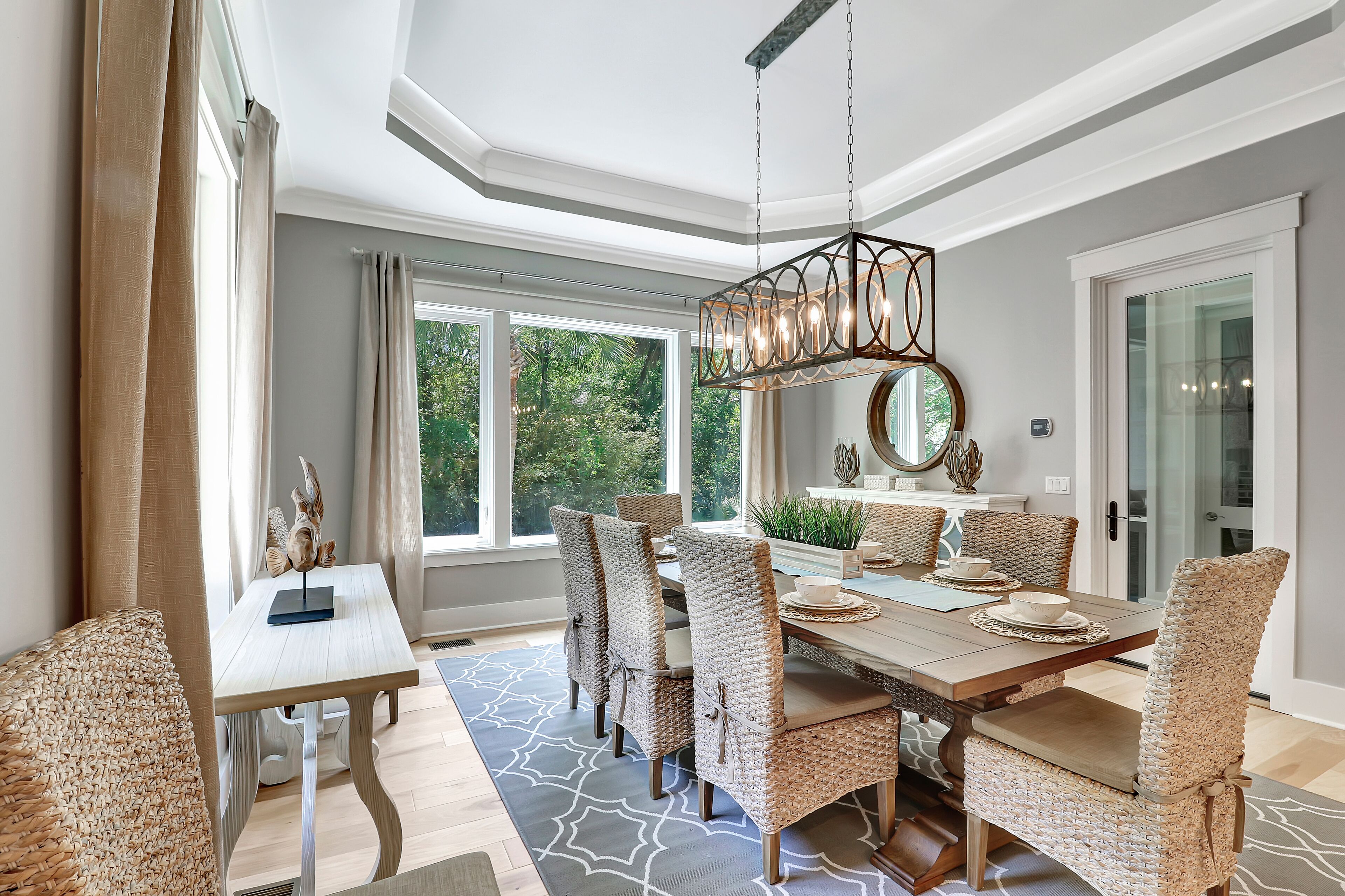 A dining area with a wooden table and wicker chairs, large windows, and a hanging light fixture.