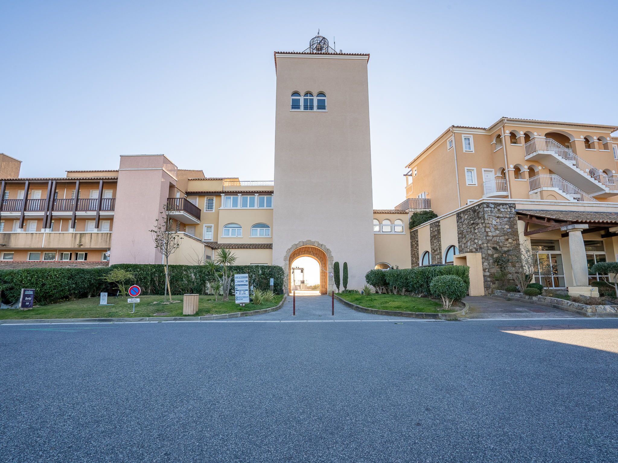 A hotel entrance with a central tower, a covered staircase, and a parking area.