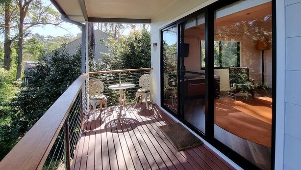 Un balcon extérieur couvert, équipé d’une table et de chaises, offrant une vue sur la verdure environnante, et une porte-fenêtre coulissante donnant accès à un espace intérieur.