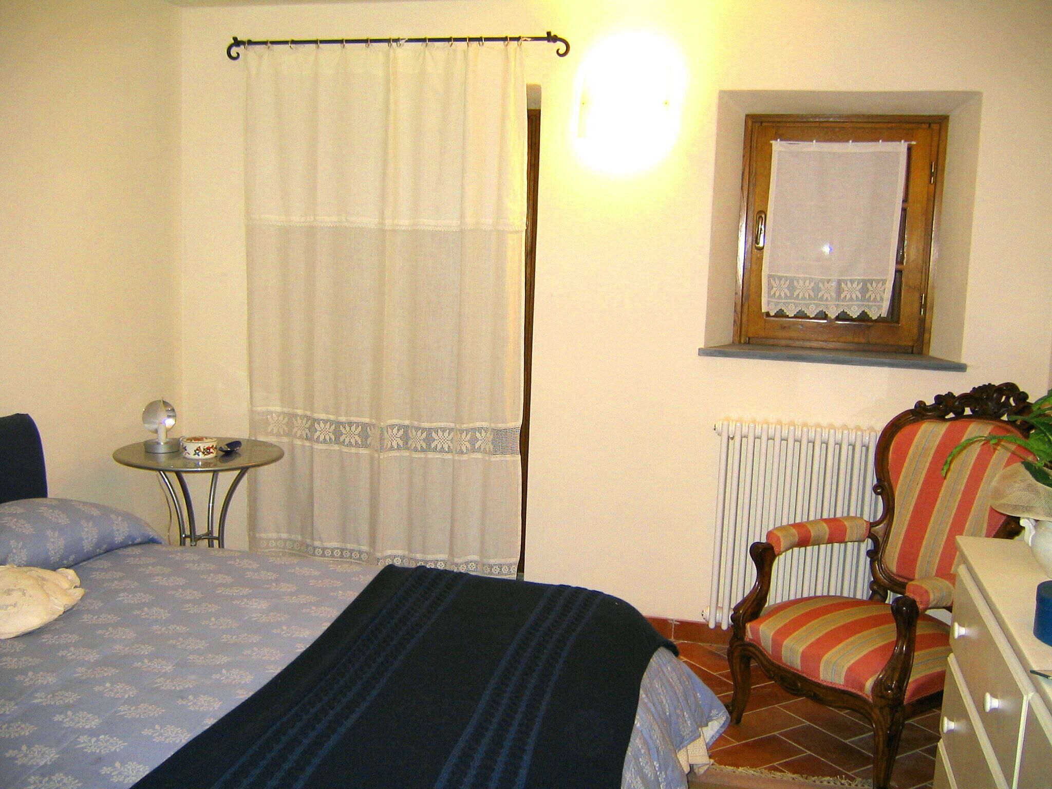 Une chambre à coucher avec un lit, une chaise, une petite table et un radiateur.