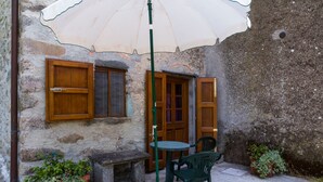 Un espace extérieur aménagé dans un style rustique, avec une table et des chaises, un banc et un pot de fleurs.