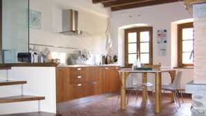 Une cuisine avec des meubles de rangement en bois, une table à manger avec des chaises et un mur en pierre.