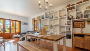 A spacious living area with a wooden dining table, a sofa, and a bench. There are white shelves with various items and a chandelier. - Can Xiroia by Interhome (Port d'Alcúdia)