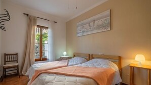 A bedroom with two beds, a window with curtains, a painting on the wall, and a small table with a lamp. - Can Xiroia by Interhome (Port d'Alcúdia)